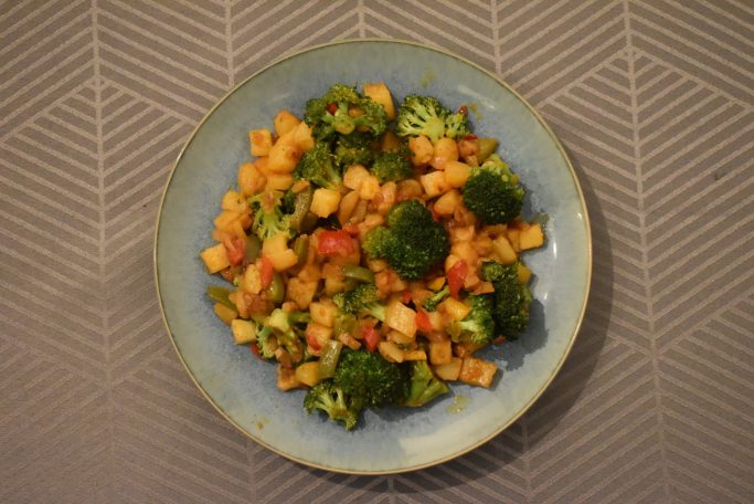 Een bord met gebakken groenten, waaronder broccoli, paprika en maïs.