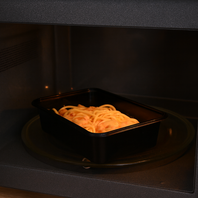 Een plastic bak met spaghetti in een magnetron.