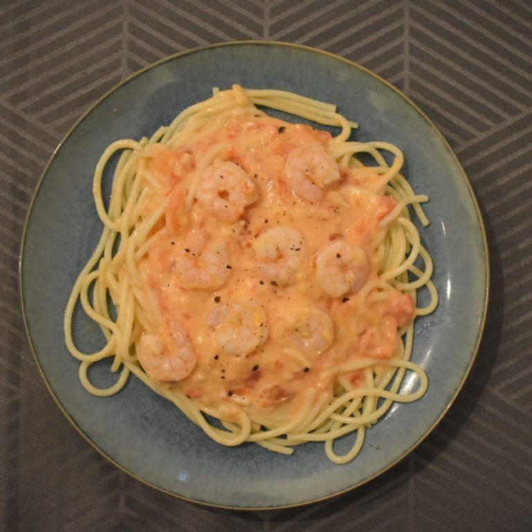 Pasta met garnalen in een romige saus, geserveerd op een blauw bord.